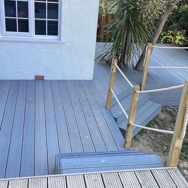 Modern grey composite decking with wooden posts and rope railing near house