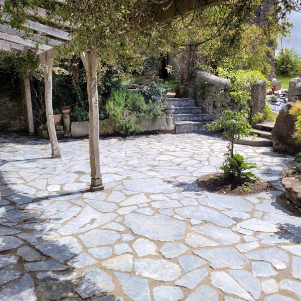 Stone patio with irregular shaped paving stones under wooden pergola in garden
