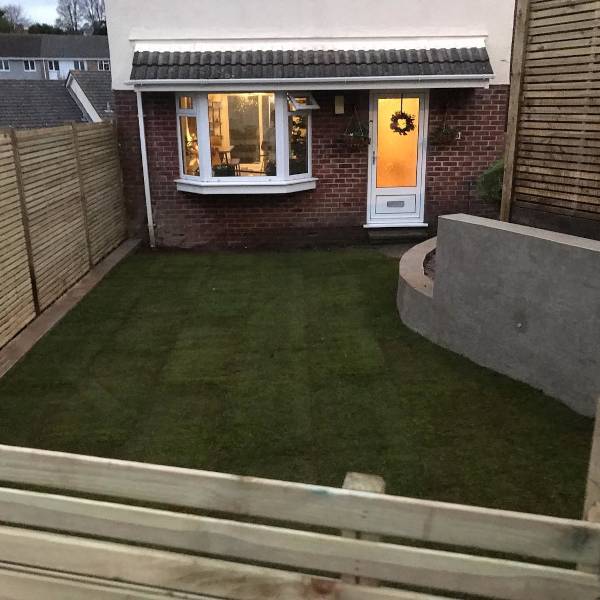 Well-maintained lawn with stone border and small greenhouse near house